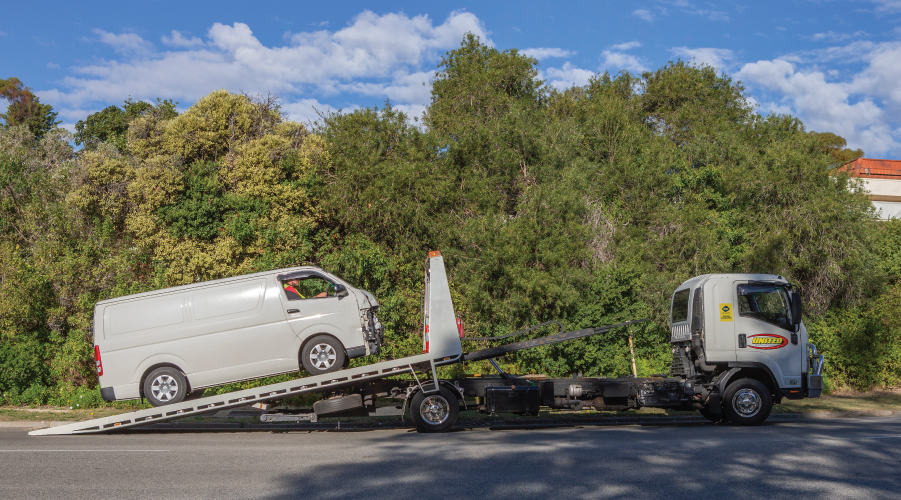 side view of a delivery van being uploaded onto a flatbed tow truck after it had been in an accident.